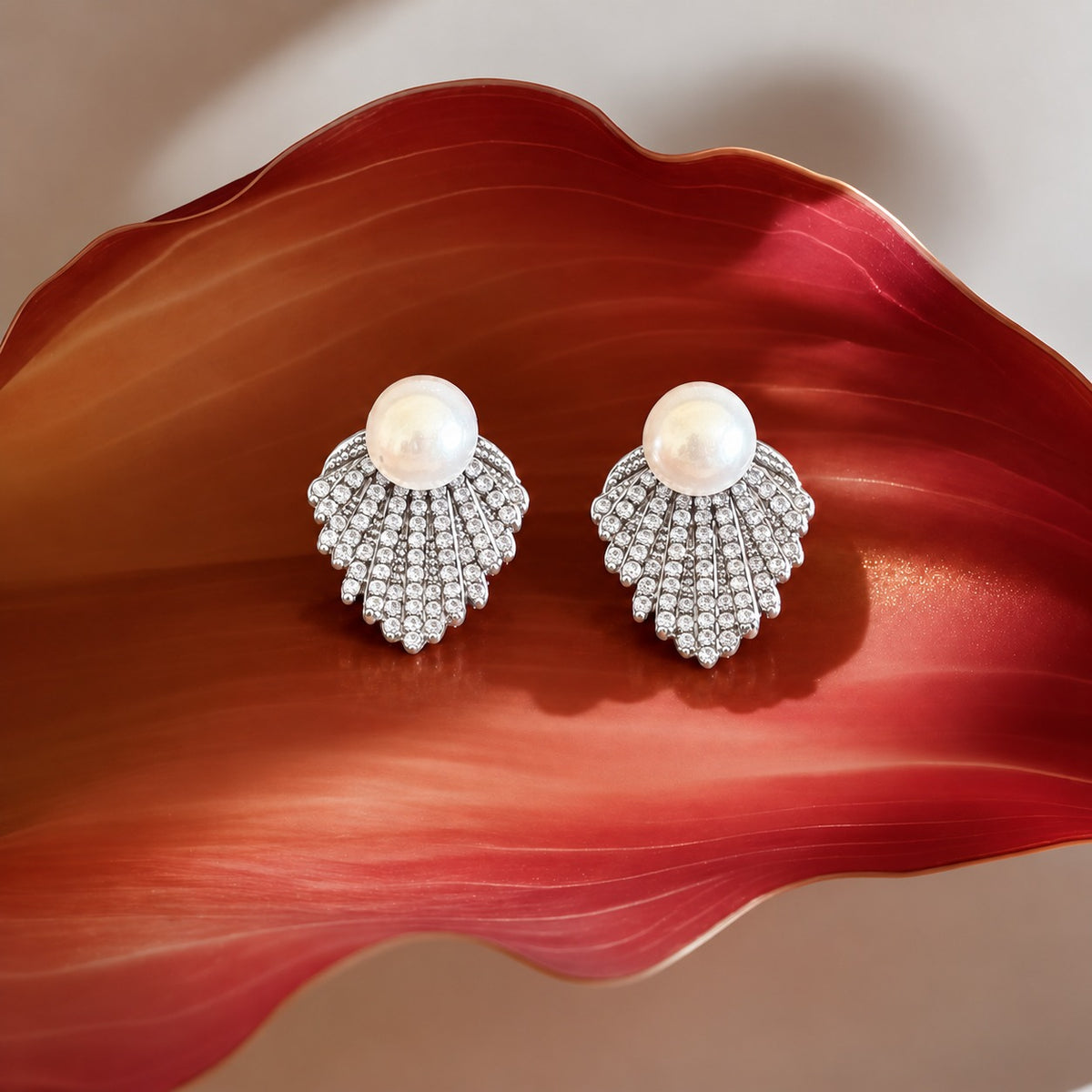 Pearl Cascade silver stud earrings with a large white pearl and graduated rows of clear zircon displayed on a deep red sculptural surface.