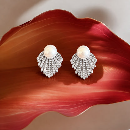 Pearl Cascade silver stud earrings with a large white pearl and graduated rows of clear zircon displayed on a deep red sculptural surface.