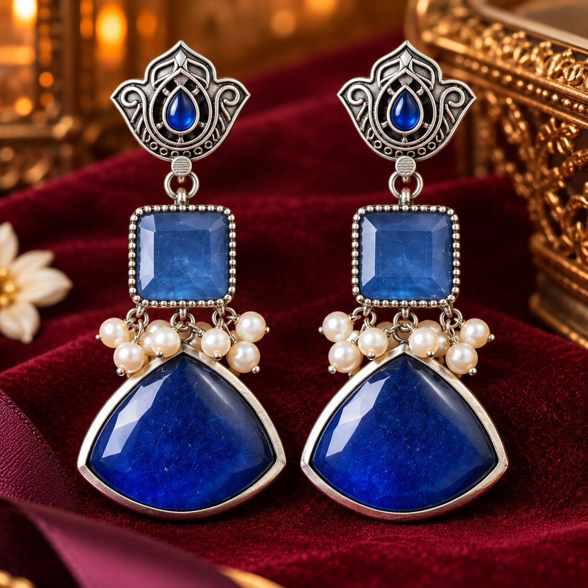 Heirloom Crest Drops in sapphire blue with silver-toned detailing and pearl accents, displayed on rich burgundy velvet.