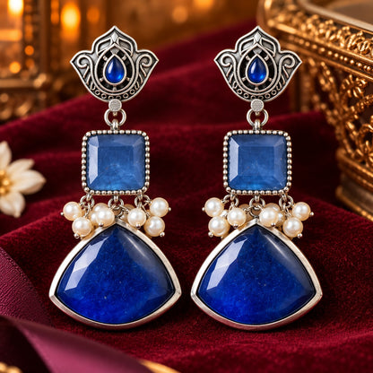 Heirloom Crest Drops in sapphire blue with silver-toned detailing and pearl accents, displayed on rich burgundy velvet.