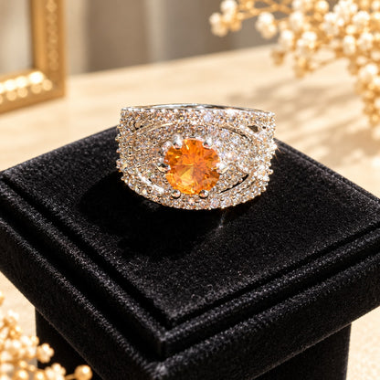 Close-up of the Amber Empress Zircon Ring showcasing its round amber-orange centre stone, clear zircon embellishments and ornate layered band on a black velvet stand