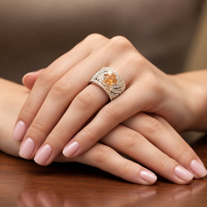 Amber Empress Zircon Ring worn on a woman's finger, featuring a vibrant amber-orange centre stone and an intricately detailed silver-tone band.
