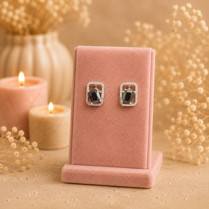 Silver geometric crystal stud earrings with rectangular faceted black gemstone displayed on a premium petal pink velvet jewellery stand with a soft luxury background.