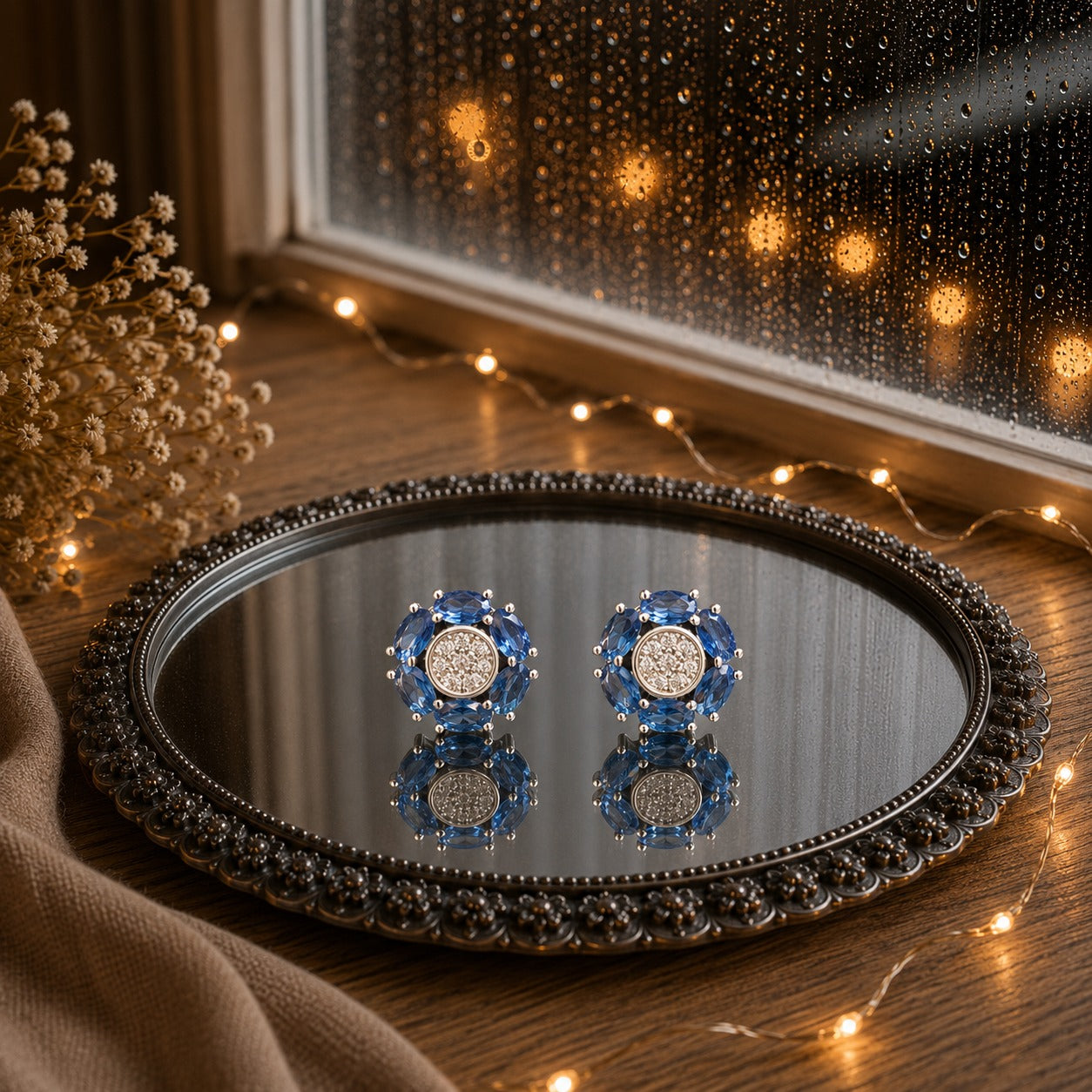 Floral crystal stud earrings with marquise-cut  blue gemstone petals and a sparkling pavé center displayed on a decorative mirrored tray in a luxury jewelry photography setting.