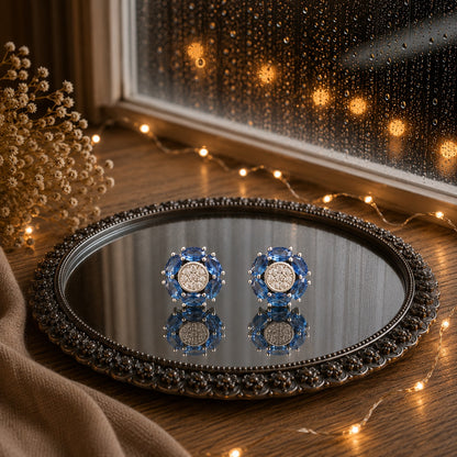Floral crystal stud earrings with marquise-cut  blue gemstone petals and a sparkling pavé center displayed on a decorative mirrored tray in a luxury jewelry photography setting.
