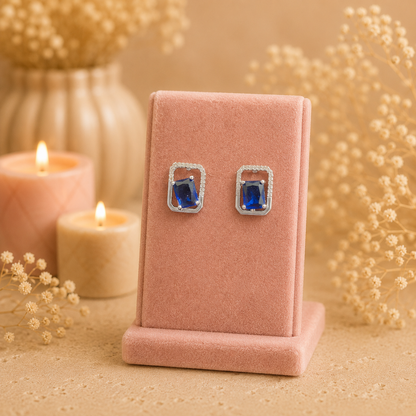Silver geometric crystal stud earrings with rectangular faceted  blue gemstone displayed on a premium petal pink velvet jewellery stand with a soft luxury background.