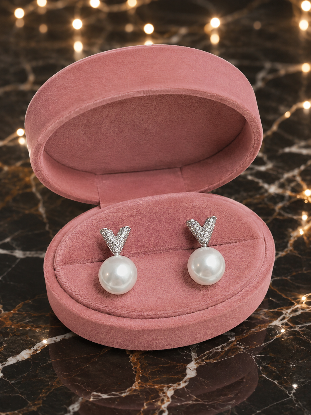 Pearl earrings with silver Y-shaped tops in a pink jewelry box on a marble surface.