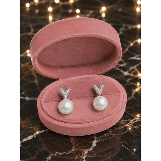 Pearl earrings with silver Y-shaped tops in a pink jewelry box on a marble surface.