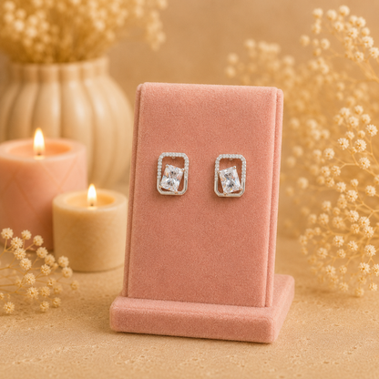 Silver geometric crystal stud earrings with rectangular faceted clear gemstone displayed on a premium petal pink velvet jewellery stand with a soft luxury background.