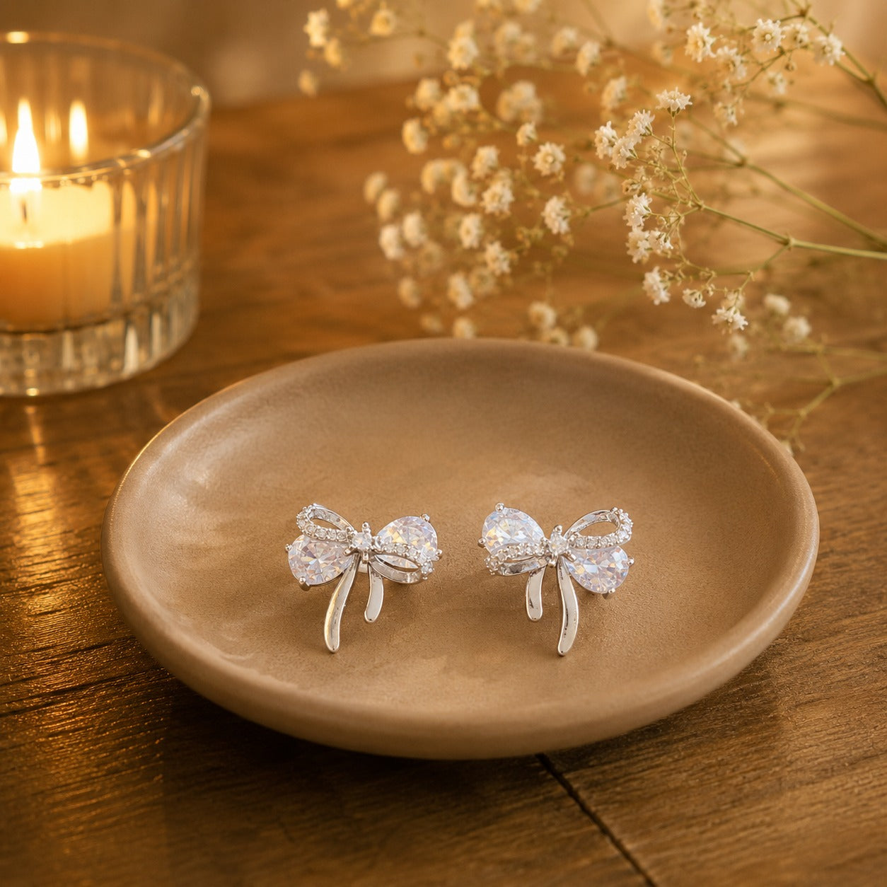 Crystal white bow stud earrings on beige ceramic plate.