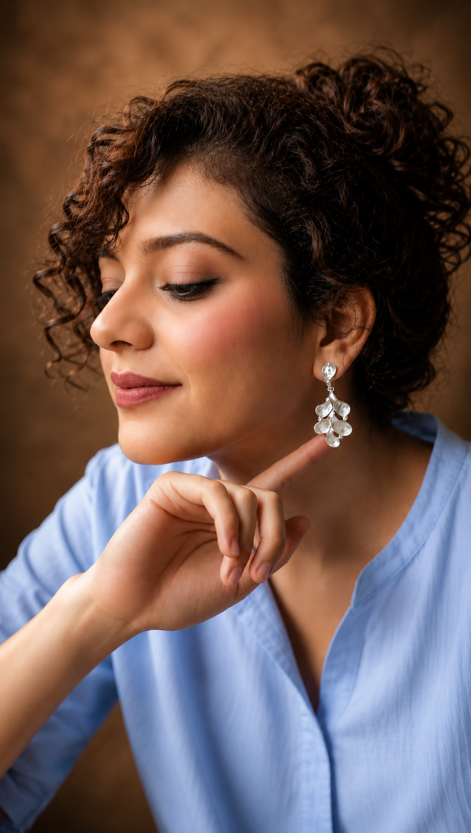 Woman wearing a blue top and floral earrings against a brown background