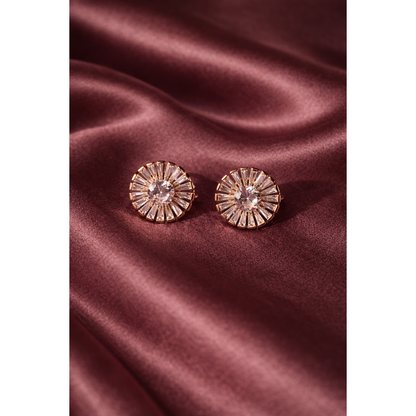 Light gold sunburst crystal stud earrings with baguette halo design placed on burnt tea pink satin cloth in luxury jewellery close-up.