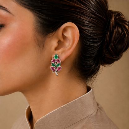 Close-up of a woman wearing a leaf-shaped earring with green and pink stones on a beige background