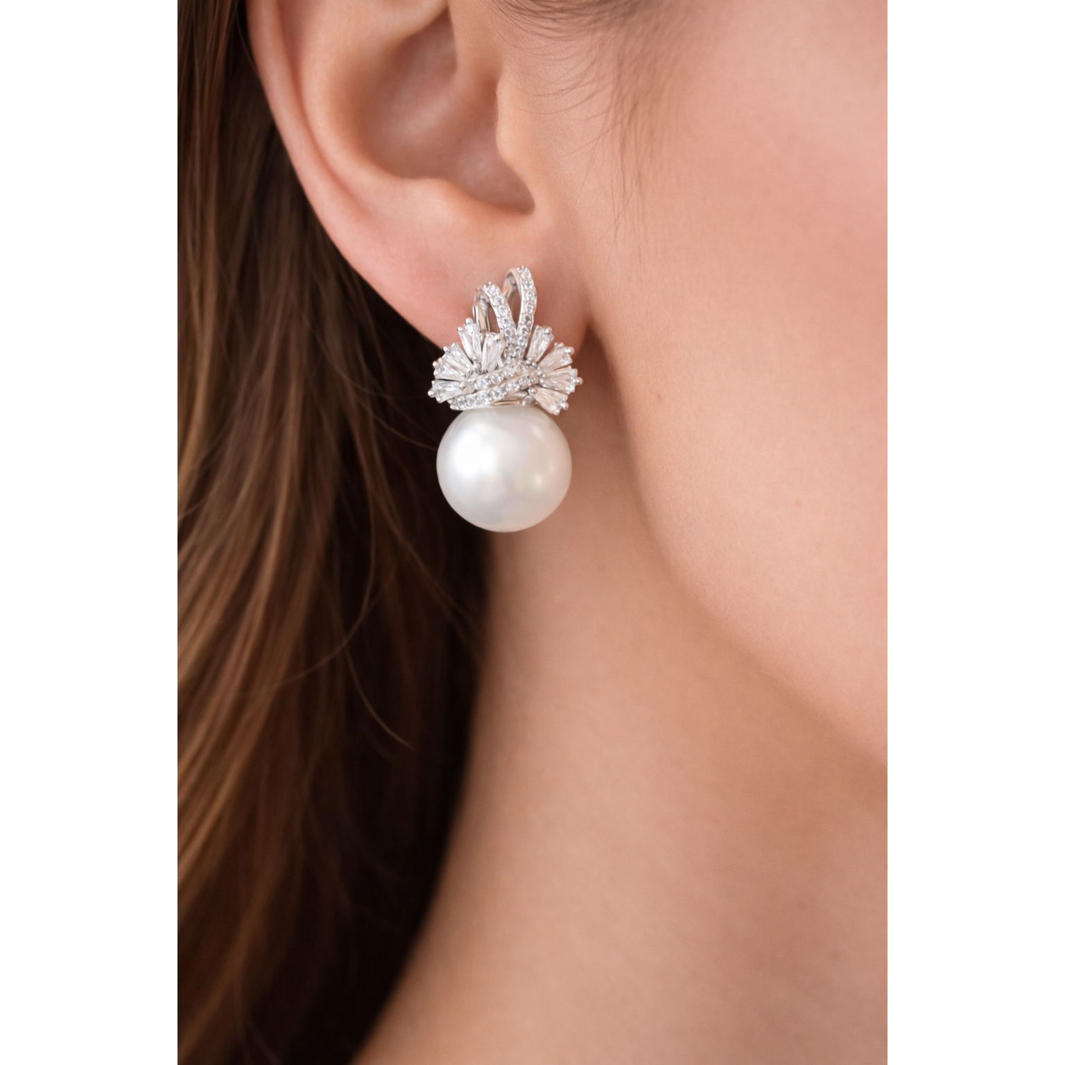Close-up of TIAS pearl drop earring with crystal design in silver finish worn on ear.