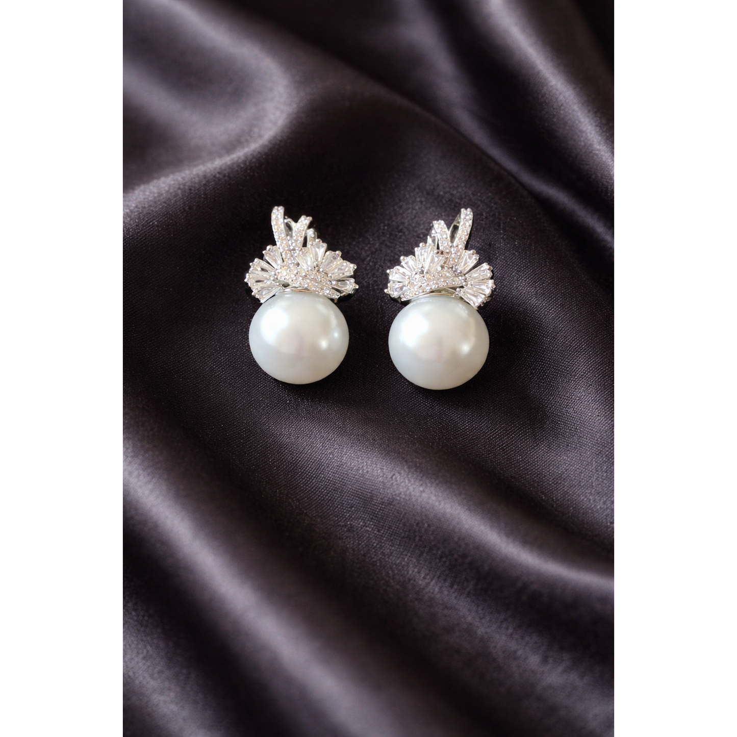Elegant TIAS silver pearl earrings with sparkling crystal accents displayed on black satin fabric