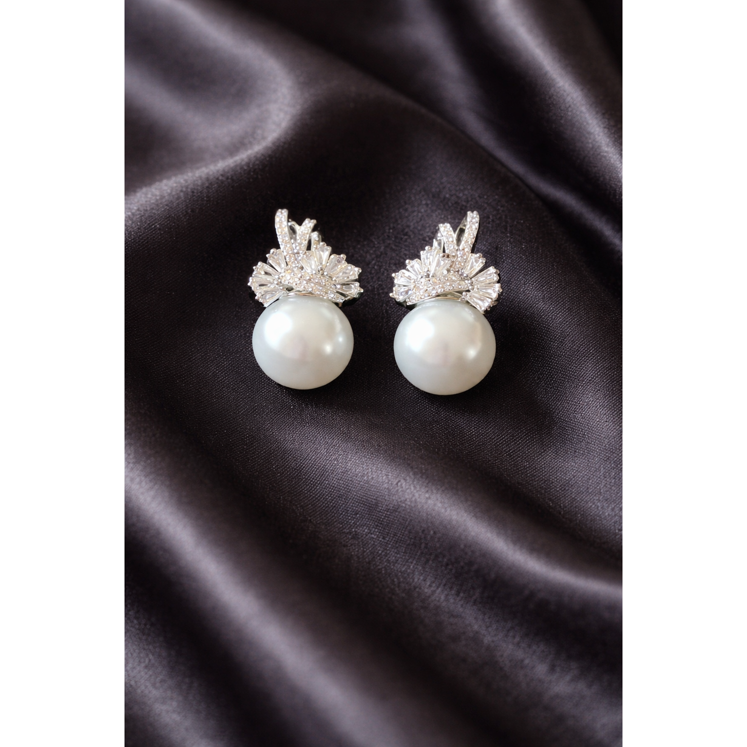 Elegant TIAS silver pearl earrings with sparkling crystal accents displayed on black satin fabric