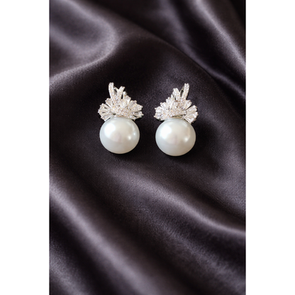Elegant TIAS silver pearl earrings with sparkling crystal accents displayed on black satin fabric