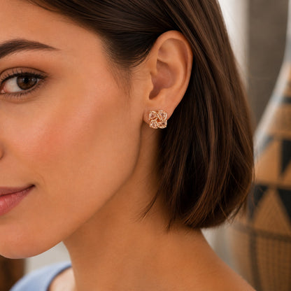 Close-up of a woman wearing four-petal crystal floral stud earrings with a polished silver or gold-tone finish.