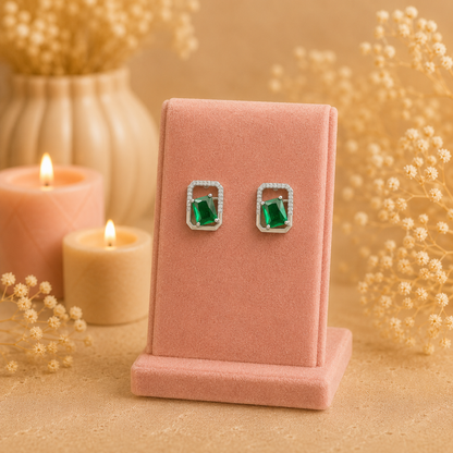 Silver geometric crystal stud earrings with rectangular faceted green gemstone displayed on a premium petal pink velvet jewellery stand with a soft luxury background.