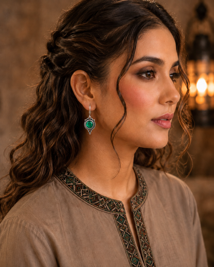 Woman wearing antique green round gemstone drop earrings with vintage detailing and embroidered taupe kurta, side profile jewellery photography.