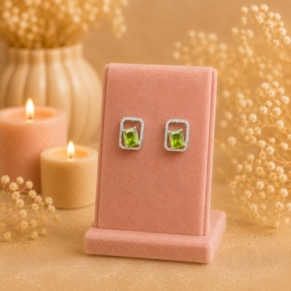 Silver geometric crystal stud earrings with rectangular faceted  lime green gemstone displayed on a premium petal pink velvet jewellery stand with a soft luxury background.