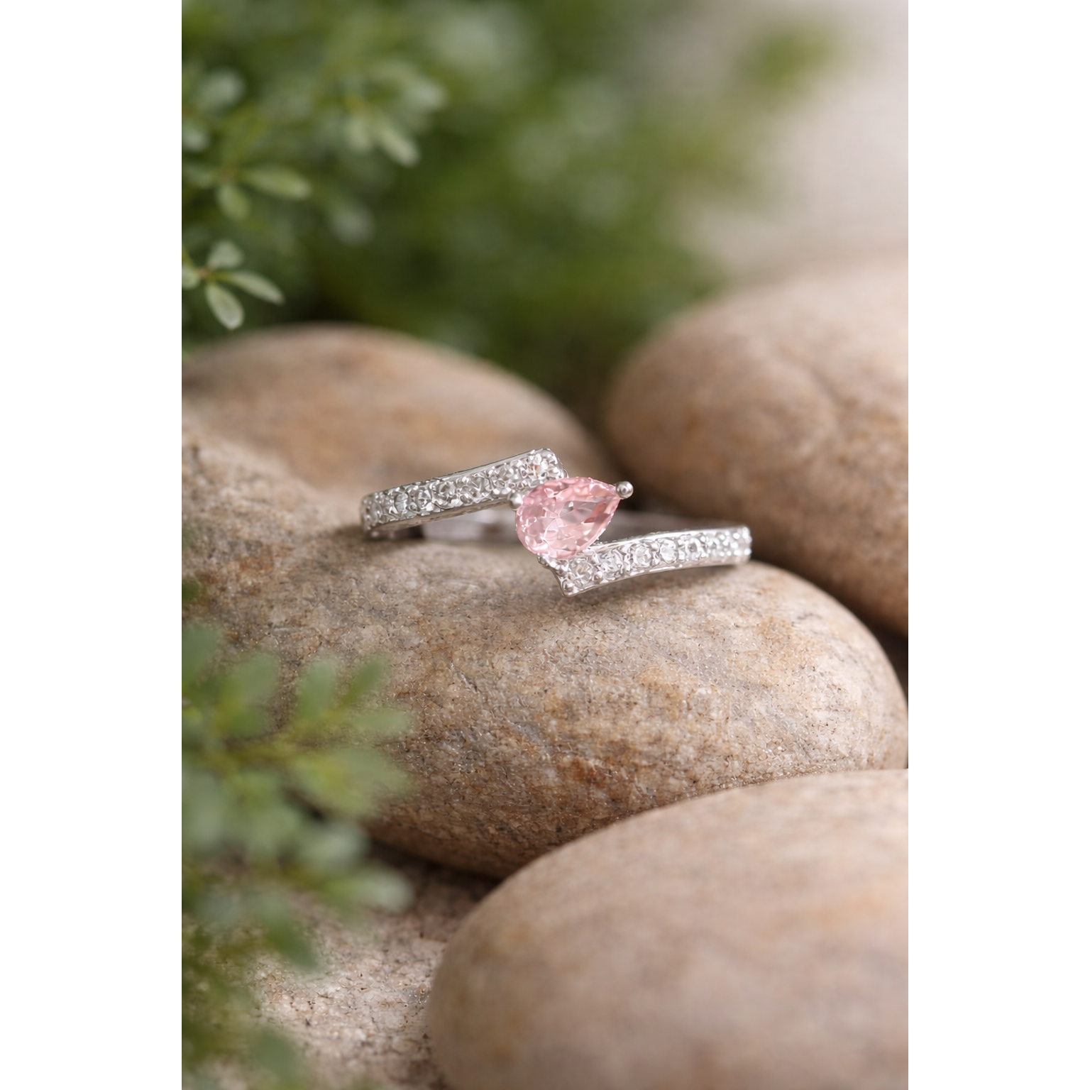 Silver ring with a soft pink gemstone on a stone surface with blurred flowers in the background