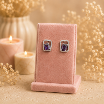 Silver geometric crystal stud earrings with rectangular faceted purple gemstone displayed on a premium petal pink velvet jewellery stand with a soft luxury background