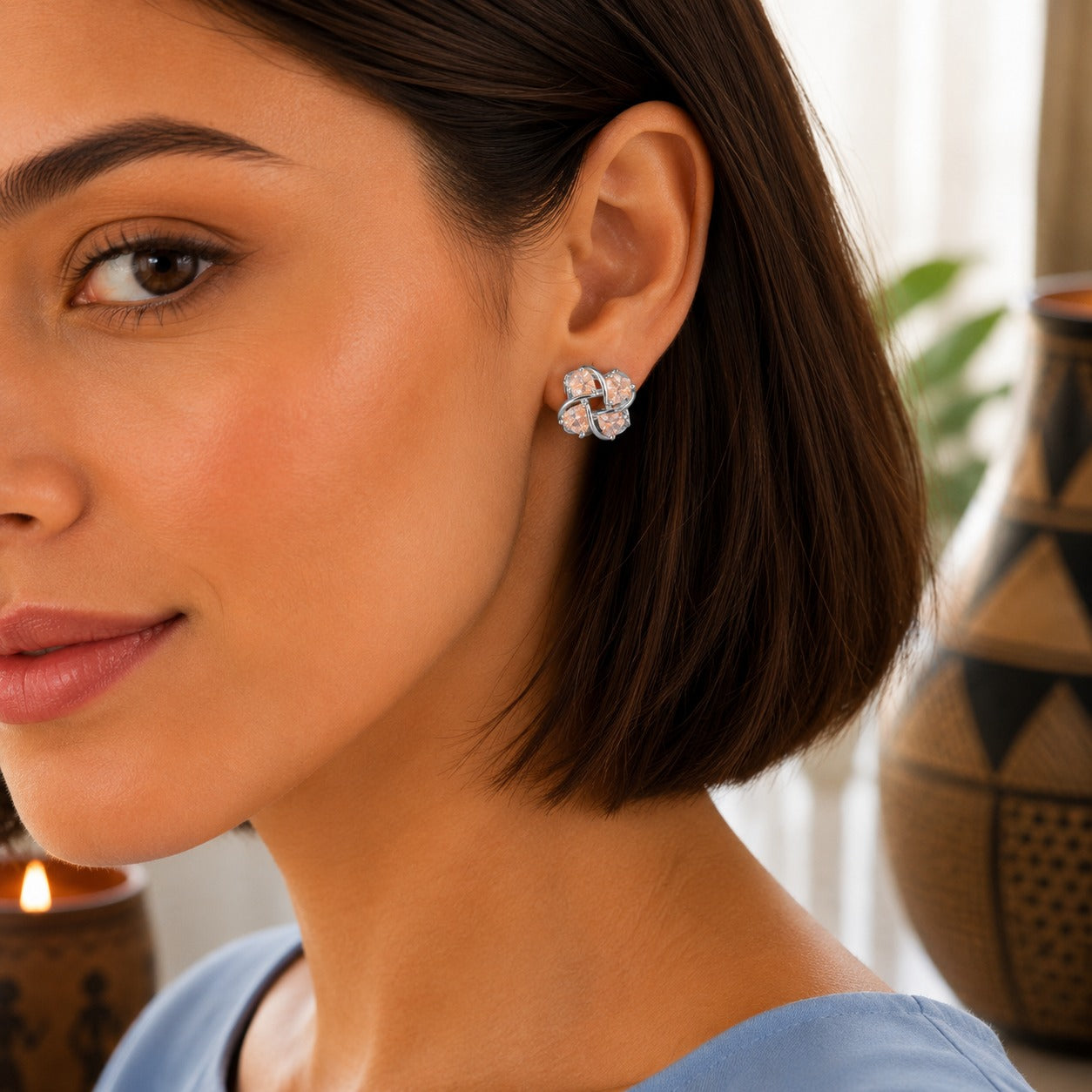 Close-up of a woman wearing four-petal crystal floral stud earrings with a polished silver or gold-tone finish.