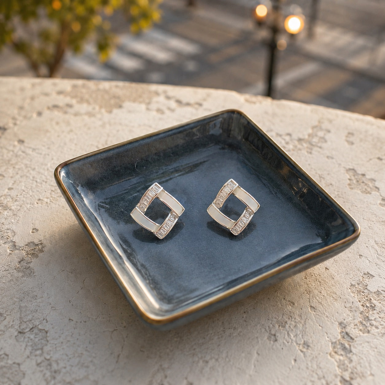 White geometric square crystal stud earrings with baguette-cut stones displayed on a premium ceramic tray in natural daylight