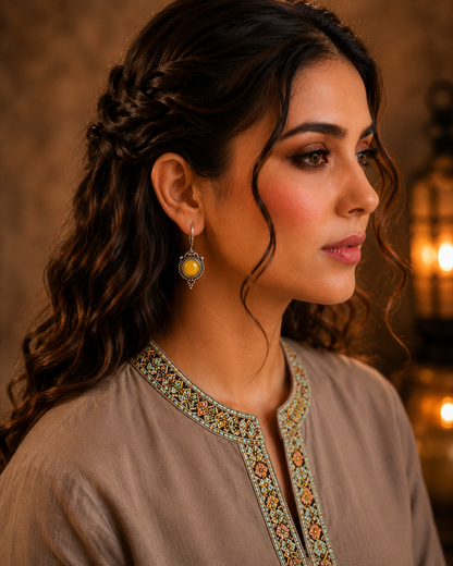 Woman wearing antique yellow round gemstone drop earrings with vintage detailing and embroidered taupe kurta, side profile jewellery photography.